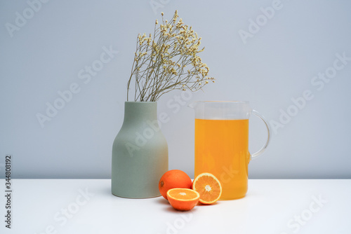 A vase with dried flowers and a glass of orange juice on the white table photo