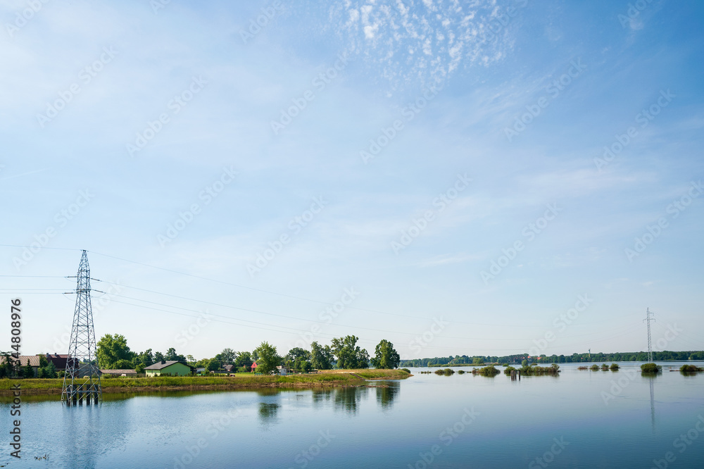 The high voltage power lines on water. Blue sky and green trees during ...