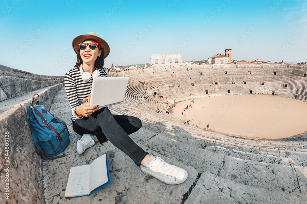 Young confident girl works with a laptop and notepad on the steps of an ancient amphitheater in Europe. Concept of teaching foreign languages and remote work as a freelancer Young confident girl works with a laptop and notepad on the steps of an ancient amphitheater in Europe. Concept of teaching foreign languages and remote work as a freelancer
