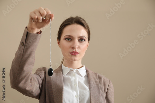 Psychotherapist with pendulum on beige background. Hypnotherapy session