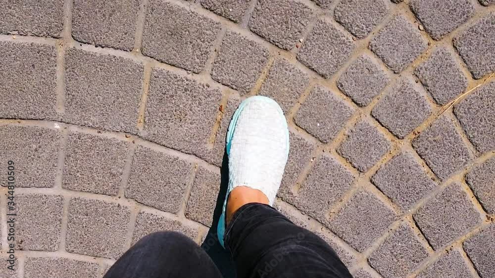 Women's legs in black jeans are on paving stones. woman in blue sports shoes, sneakers is walking on street, road. Close-up. Slow motion. Women's legs in black jeans are on paving stones. woman in blue sports shoes, sneakers is walking on street, road. Close-up. Slow motion.