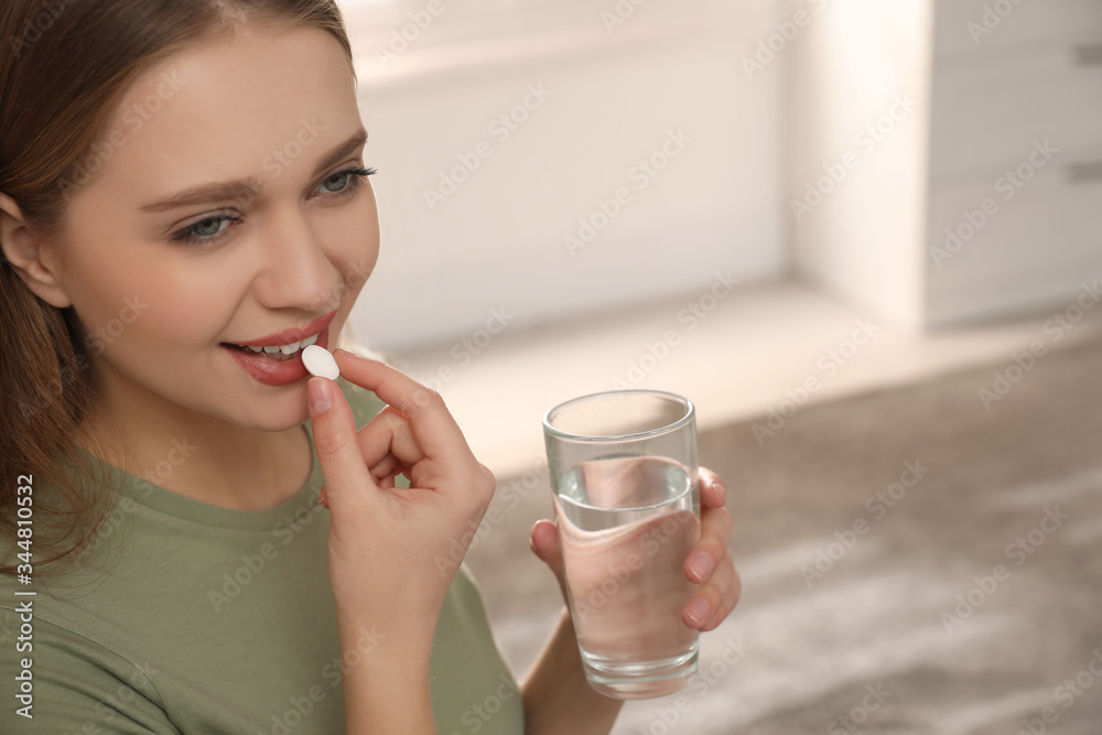 Young woman with glass of water taking vitamin pill at home Young woman with glass of water taking vitamin pill at home