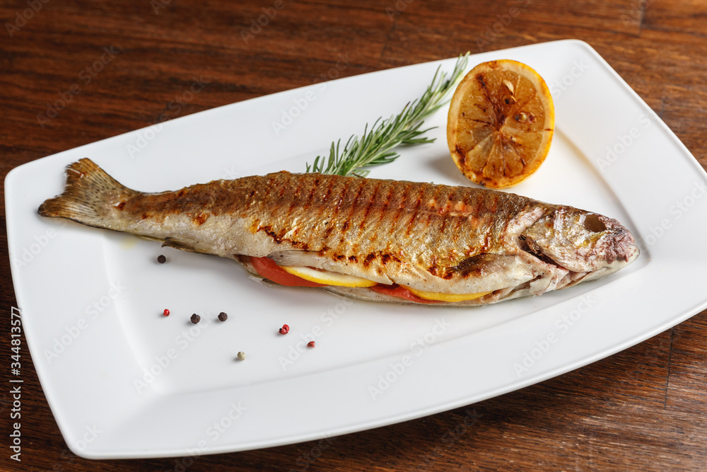 Grilled trout with resemary and lemon served on a white plate Grilled trout with resemary and lemon served on a white plate