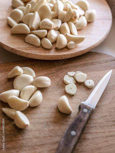 one cut and many uncut peeled cloves of garlic on wooden cutting boards, knife