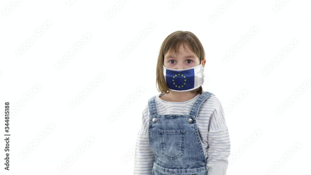 Charming girl, blonde posing on a white background. Quarantine, virus and pandemic concept. On the child a protective medical mask with the flag of the European Union. Different emotions and gestures. Charming girl, blonde posing on a white background. Quarantine, virus and pandemic concept. On the child a protective medical mask with the flag of the European Union. Different emotions and gestures.