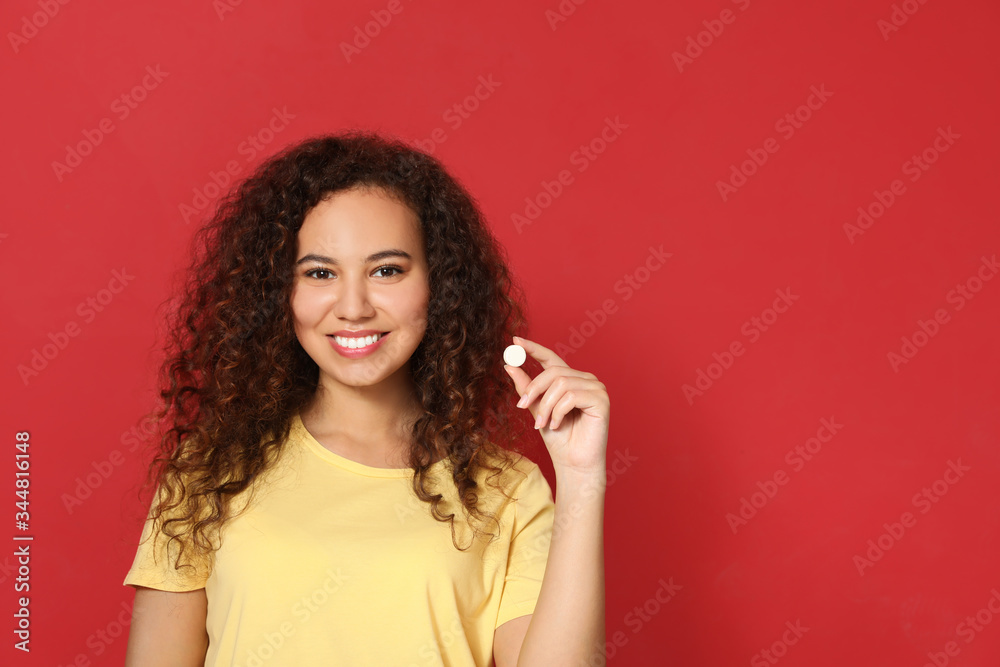African-American woman with vitamin pill on red background. Space for text African-American woman with vitamin pill on red background. Space for text