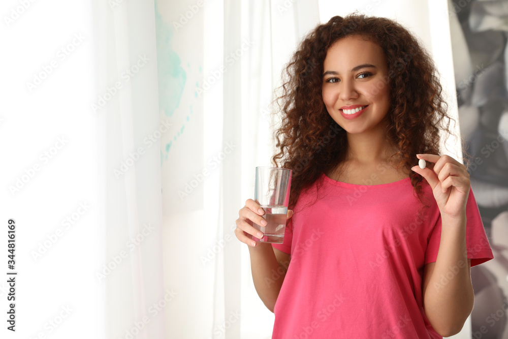 African-American woman with glass of water and vitamin pill indoors. Space for text African-American woman with glass of water and vitamin pill indoors. Space for text