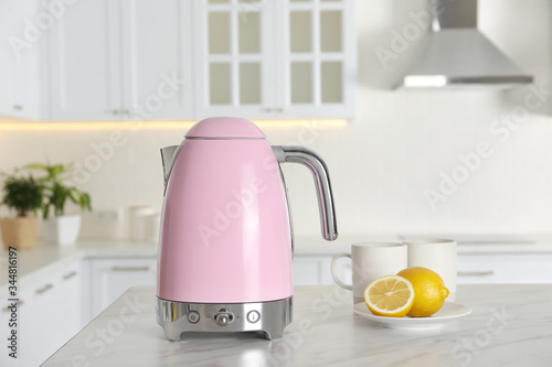 Modern electric kettle, cups and lemons on table in kitchen