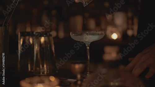 Handheld real time close up shot of a bartender pouring a cocktail into a glass at a bar in Bangkok, Thailand.