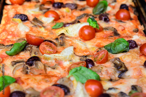 Traditional Italian pizza with fresh tomatoes, artichoke, mushrooms and olives displayed for sale at a street food market festival in Bucharest, Romania, healthy food photographed with soft focus 