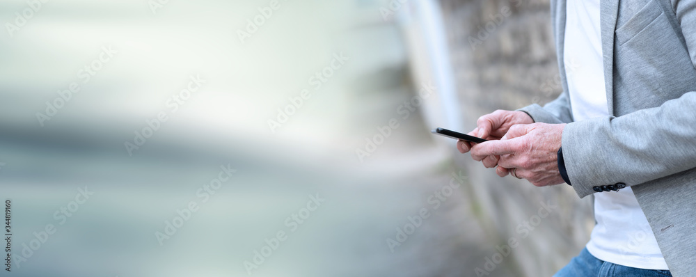 Man standing against a wall and using mobile phone; panoramic banner