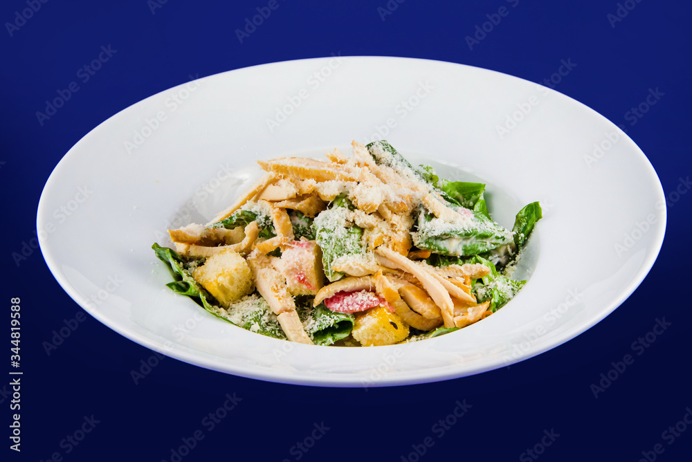 Plate with fresh caesar salad. Closeup on a white plate on a blue background. Plate with fresh caesar salad. Closeup on a white plate on a blue background.