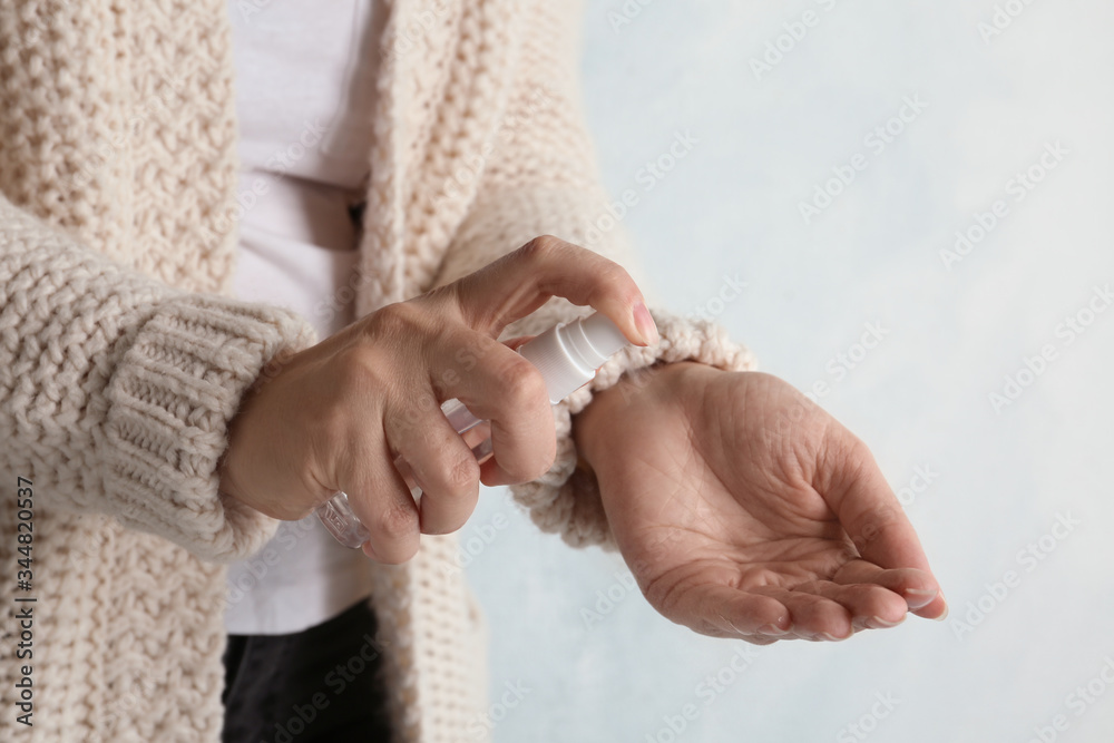 Woman spraying antiseptic onto hand against light background, closeup. Virus prevention