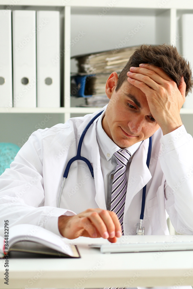 Thoughtful male doctor press key on computer pc keyboard at workplace in office portrait. Medic instrument shop, modern communication, surfing, remote aid, reading news, exams preparation concept