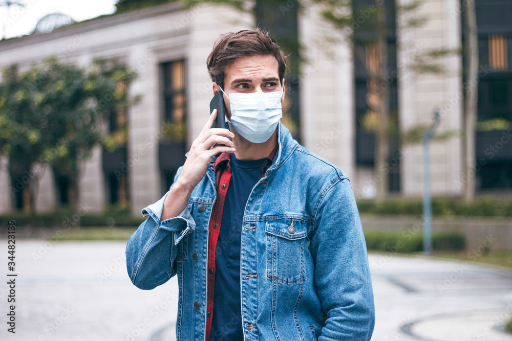 Obraz premium A mature handsome man with a beard talking on his mobile phone and wears a face pollution mask to protect himself from coronavirus on the street.