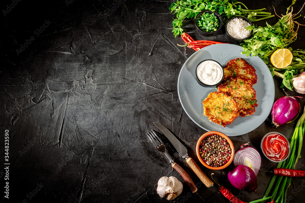 Potato pancakes with sour cream, herbs, garlic and spices on a dark background. Top view with copy space