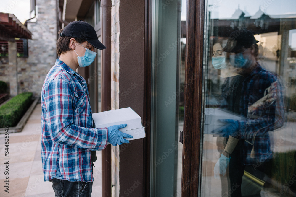 Courier in protective mask delivers parcel, customer in medical gloves receives box. Delivery service under quarantine, disease outbreak, coronavirus covid-19 pandemic conditions.