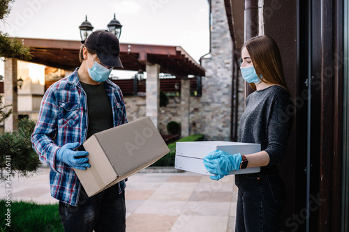Courier in protective mask and medical gloves delivers takeaway food. Delivery service under quarantine, disease outbreak, coronavirus covid-19 pandemic conditions.