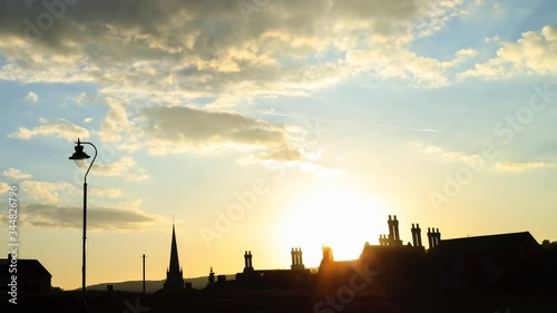 Timelapse of sun going down and street light coming on over English market town buildings and chimneys. 
