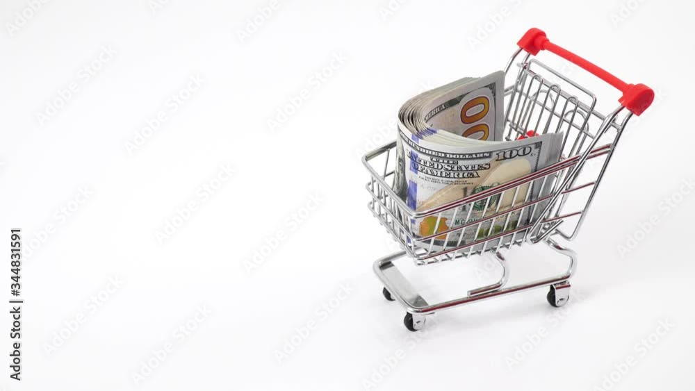 Hand pushing miniature toy supermarket trolley. In a cart a bundle of one hundred dollar bills. A lot of money goes to a supermarket or shopping mall. Expensive luxury shopping concept.
