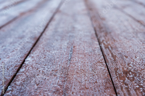Brown boards covered with frost. Wooden background with blur in perspective. Wood texture with frost. Floor boards on the terrace arranged in parallel.