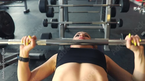 Attractive fitness girl with long hair is doing exercies with barbell. Body building female in the gym. She is wearing in black top.