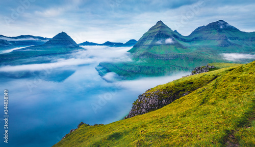 Dramatic morning view of Faroe Islands with low clouds, Denmark, Europe with low clouds. Adorable summer scene of Eysturoy island, Funningur village location. Beauty of nature concept background.