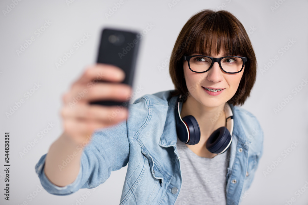 portrait of beautiful young woman or teenage girl with braces on teeth taking selfie photo with smartphone over gray