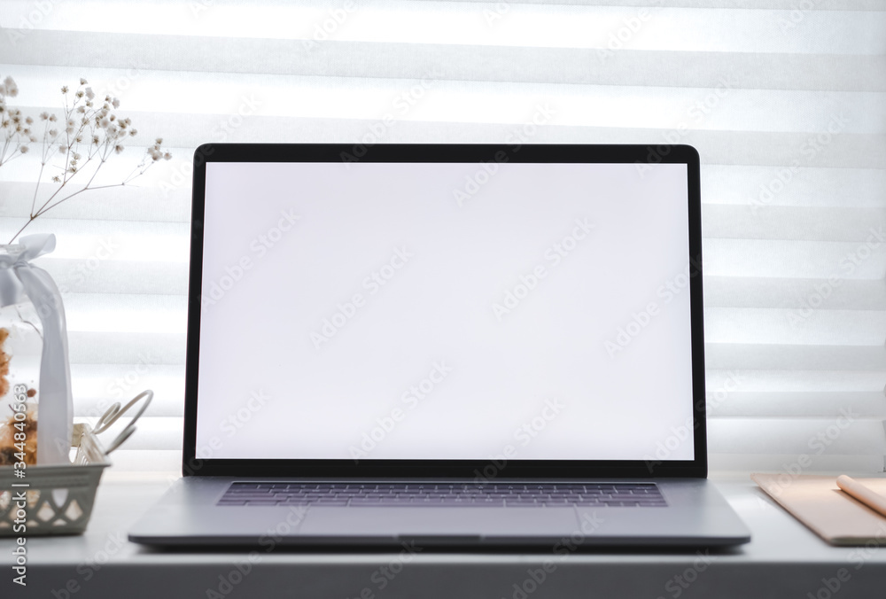 A laptop with a white blank screen and a notebook on the window on a sunny day. Workplace home, mock up. A laptop with a white blank screen and a notebook on the window on a sunny day. Workplace home, mock up.