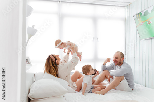 A young happy family with young children lying around, hugging, laughing on the bed at house