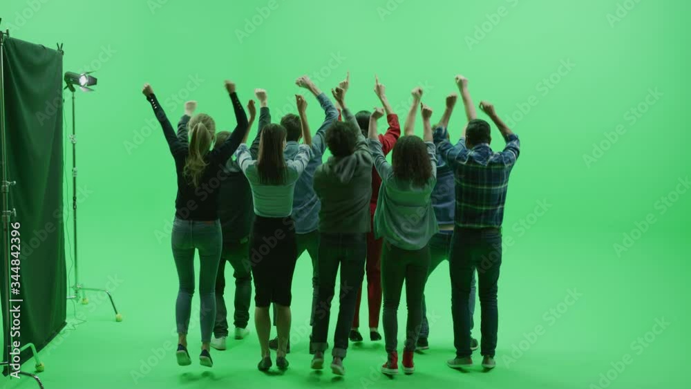 Green Screen Chroma Key Studio: Two Rows of Nine Diverse Fans Cheering, Jumping, Applauding with Hands in the Air at the Public Sport Event, Concert, Festival, Party. Back View Full Shot. Slow Motion