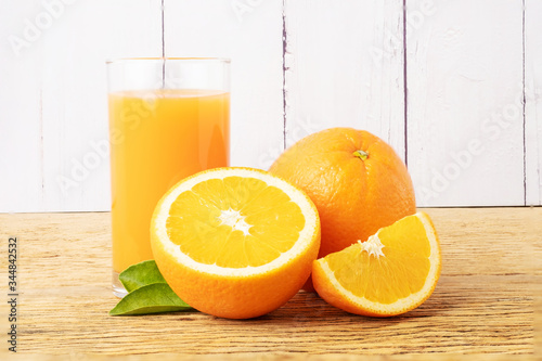 Glass of fresh orange juice with fruits cut in half and sliced with green leaf on wood background