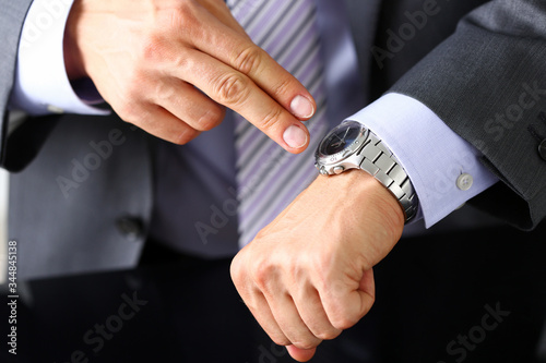Man in suit and tie check out time at silver wristwatch closeup. Show and point with finger, waste minute, modern punctual life style, start hurry, job idea, last second, clockwork precision concept