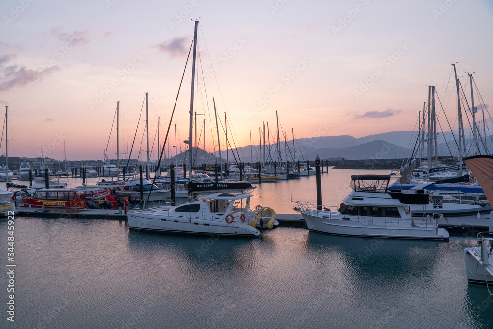 Sunset Marina. Boats & yachts docked at sea. Airlie beach boat harbour waterfront sunset view. Reflections in water. Mountain landscape background. Whitsundays Islands, Queenstown, Australia