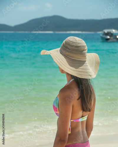 Woman on paradise blue beach. Tourist on Whitsundays beach, white sand, in pink bikini & hat, with aqua turquoise ocean. Travel, holiday, vacation, paradise, exotic. Whitsundays Islands, Australia. © Jam Travels