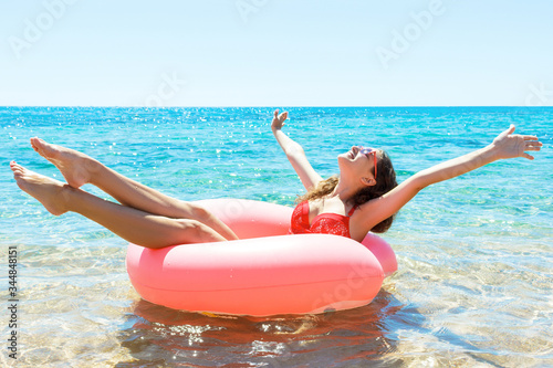 Pretty girl is having fun on a pink inflatable ring in the sea. Relaxation at the beach