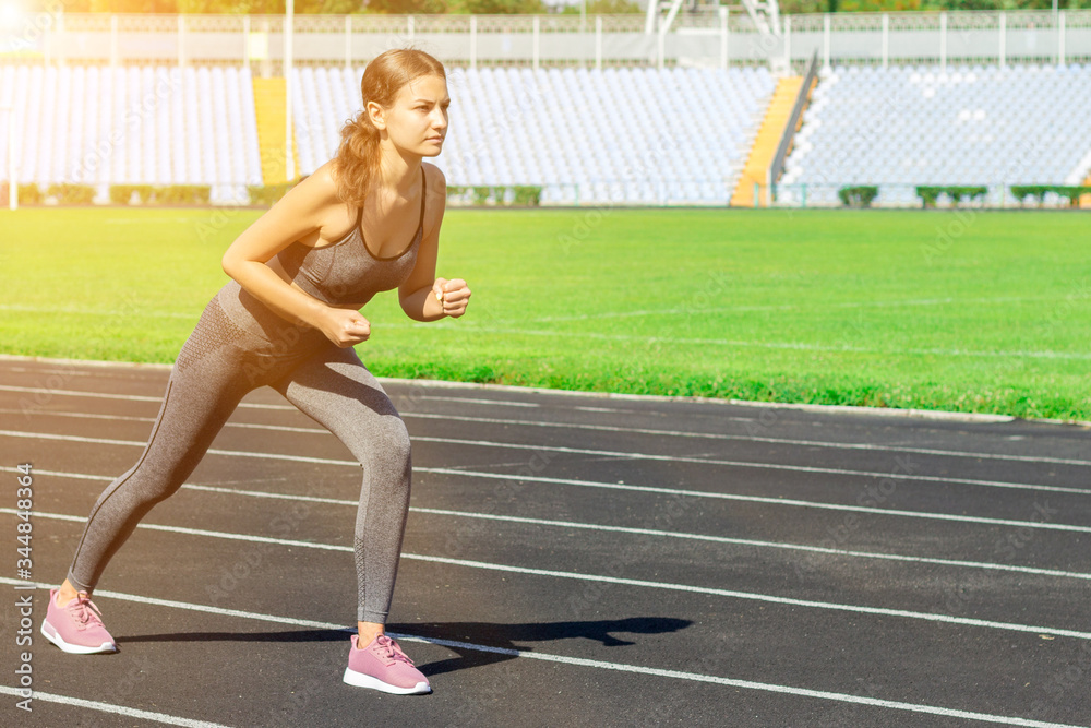 Young athlete is getting ready to start running on a track. Woman is preparing for competition at the stadium Young athlete is getting ready to start running on a track. Woman is preparing for competition at the stadium