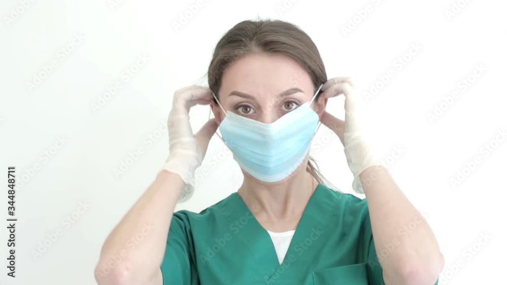 Female doctor or nurse is preparing to receive patients during an epidemic on a white background. She puts on a medical mask, goggles, a disposable cap. Close up porttrait Female doctor or nurse is preparing to receive patients during an epidemic on a white background. She puts on a medical mask, goggles, a disposable cap. Close up porttrait