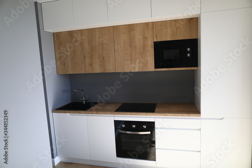 Closeup of kitchen interior in new apartment. Small and compact furniture for flat. Modern black cookstove sink and microwave. Design and renovation concept