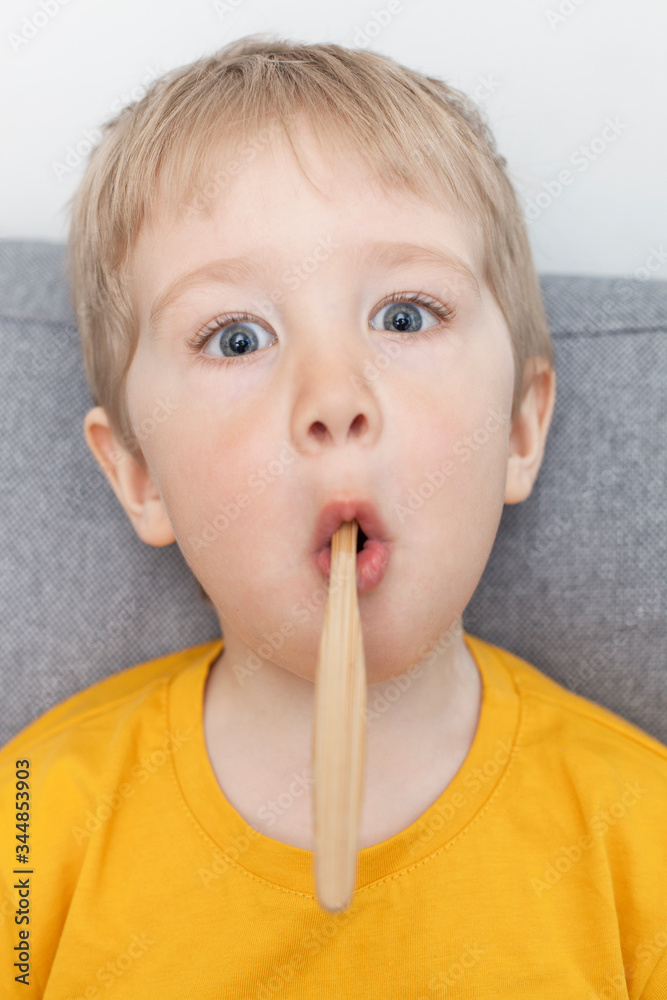 Little blond boy indulges with a bamboo brush in his mouth Little blond boy indulges with a bamboo brush in his mouth