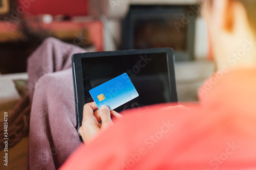 Woman lying on the sofa and shopping online from home with her tablet and credit card