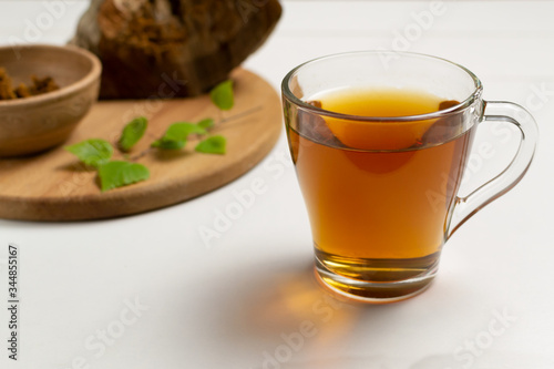 Tea in a glass cup and chaga mushroom on a wooden board on a white background. Horizontal orientation