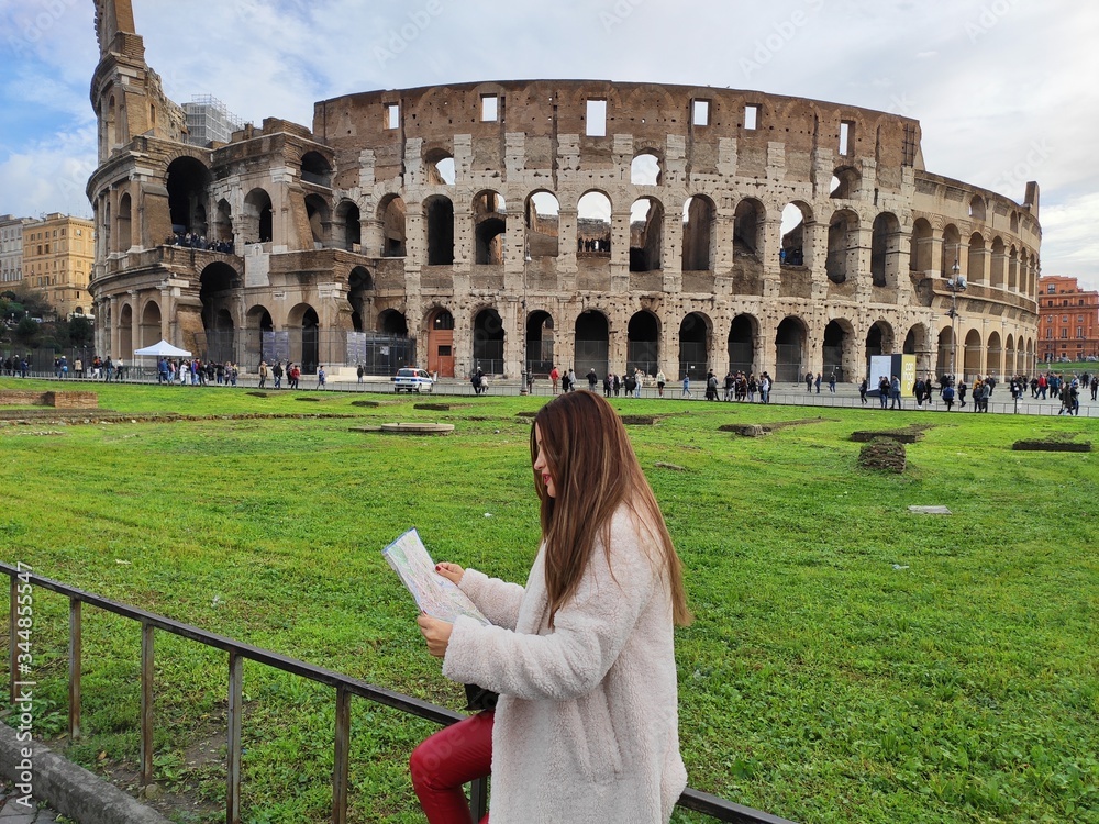 Young girl with white coat looking information in a map about Coliseum, Rome, Italy