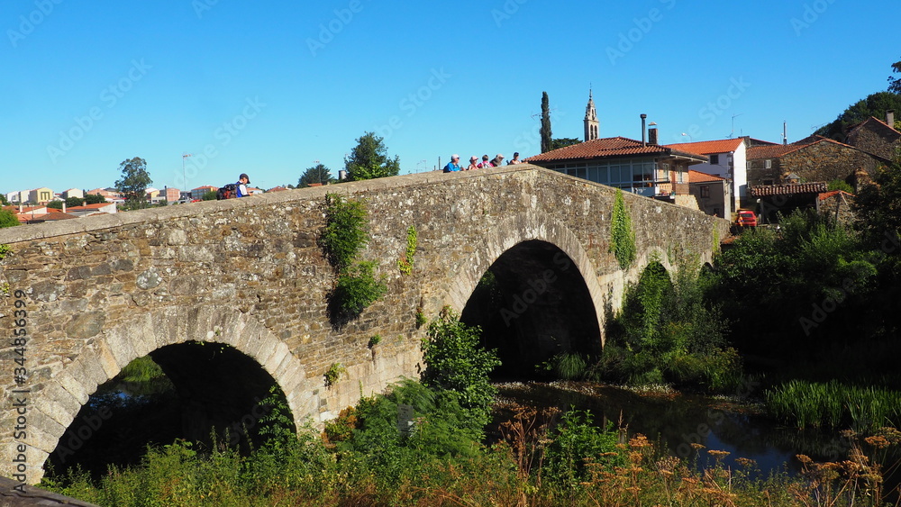 puente medieval de cuatro ojos sobre el rio furelos, al fondo el campanario de la iglesia del pueblo, mellid, la coruña, galicia, españa, europa