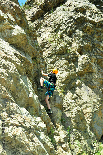  A teenager in climber equipment climbs a cliff.