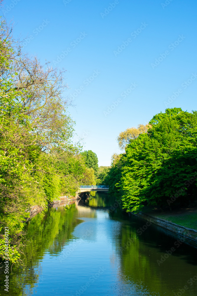 Landschaftsaufnahme mit einer Brücke im Hintergrund und einem Fluss im Mittelpunkt, daneben Wälder und Bäume im saftigen Grün
