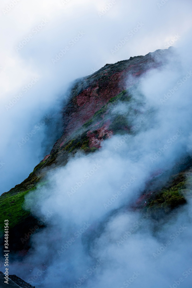 Steam rises from Icelandic hot springs with sulphur turning rock a green and red colour.