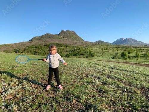 A child girl plays in nature. Active summer sport for children on the grass. Children's badminton. Little girl have fun in the fresh air.