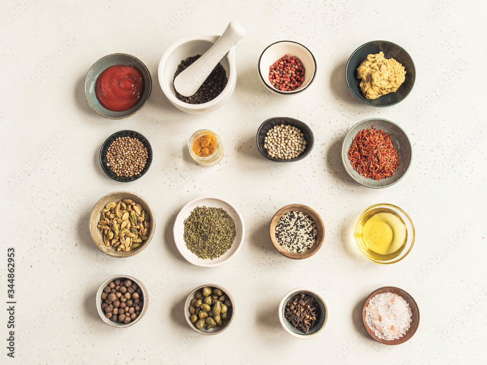 Various dry spices and sauces on a light background. Flat lay of small bowls with dijon mustard, olive oil, ketchup, capers and spices. Top view