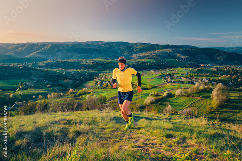 Male runner training in spring morning nature. Man running up hill. Beautiful spring scenery in background. Hrinova village in Slovakia